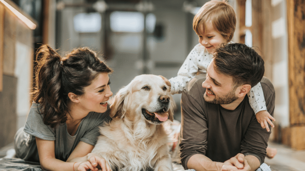 A family with a smiling young child and a happy golden retriever lying together on the floor.
