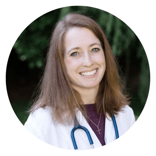 A smiling person with shoulder-length hair, wearing a lab coat and a stethoscope around their neck.