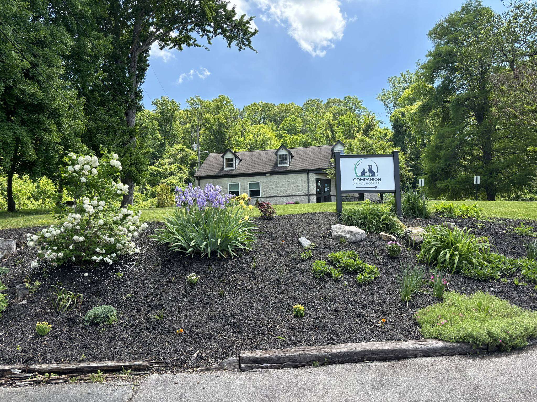 A small house with a sign reading "Companion." Surrounded by a garden bed with various plants and trees in the background.